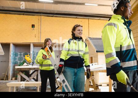 Smiling young female vocational student walking in workshop towards training session with friends at school Stock Photo