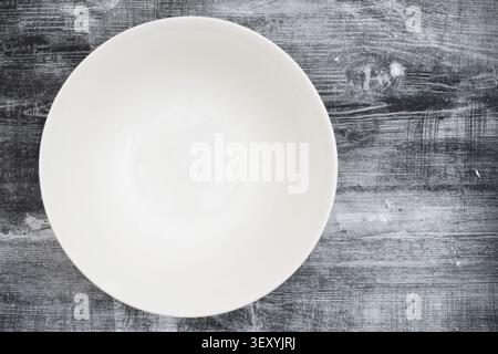 Minimal white ceramic bowl centered on rustic gray wooden background representing food serving, kitchen table setting, and clean minimal design. Stock Photo