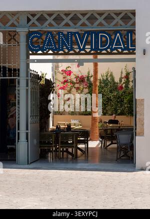 Alcudia Mallorca Spain. 30.05..2026.  A man sits alone at a table in a sunlit outdoor restaurant patio adorned with vibrant pink bougainvillea flowers Stock Photo