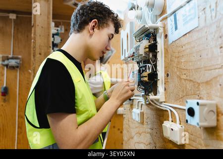 Young male student inserting electrical wiring into open terminal block components mounted on wooden mockup board in wor Stock Photo