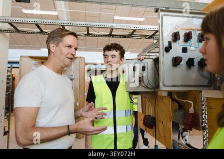 Mature male instructor teaching about electrical components to students at workshop in vocational school Stock Photo