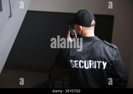 Bodyguard in uniform using walkie talkie while walking down stairs indoors, space for text Stock Photo