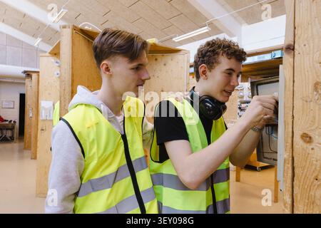 Two vocational students wearing reflective vest working together while connecting wiring inside open electrical control Stock Photo