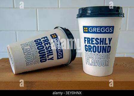 Two used Greggs Coffee Mugs or cups with Freshly Ground Fairtrade Coffee printed on the front, one on it's side on wooden counter Stock Photo