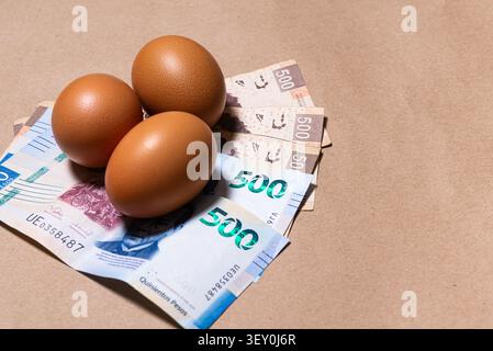 Three brown eggs resting on Mexican peso bills symbolizing food costs and inflation. Stock Photo