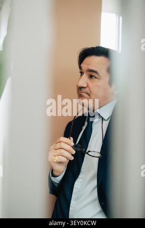 Thoughtful businessman looking away while holding eyeglasses in hand at office Stock Photo