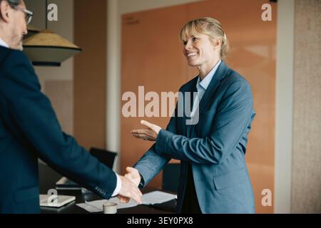 Happy female executive shaking hands with male colleague after successful meeting Stock Photo