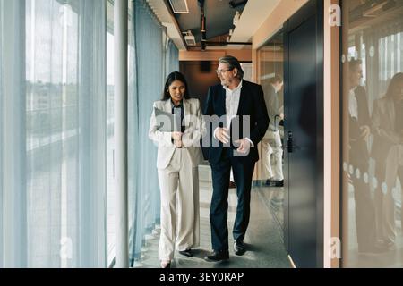 Full length of diverse business colleagues discussing while walking in modern office hallway Stock Photo
