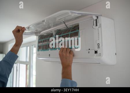 Man's hands open wall-mounted air conditioner to remove dusty filter, cooling system maintenance. Stock Photo