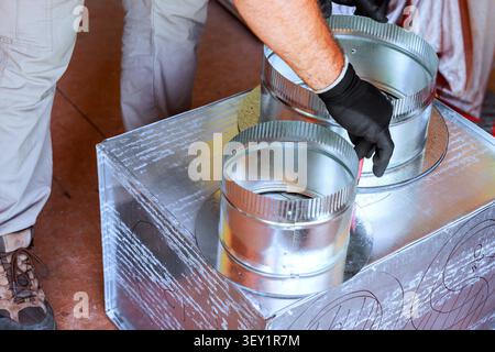 Contractor is fitting metal ducts to large box while working on heating cooling system indoors Stock Photo