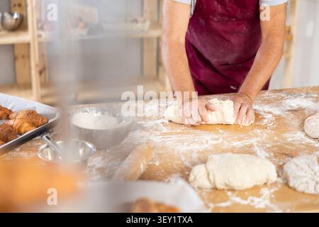 Unrecognizable senior man works in bakery as baker, kneads dough, works with flour. Stock Photo