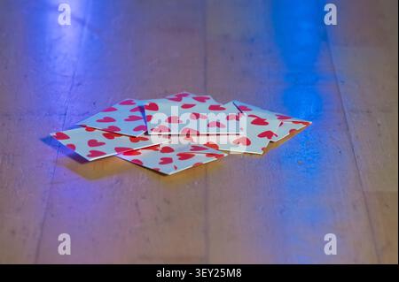 Scattered heartpattern cards on wooden floor, neonblue and pink reflections casting soft glow, lowangle closeup capturing quiet aftermath of latenight Stock Photo