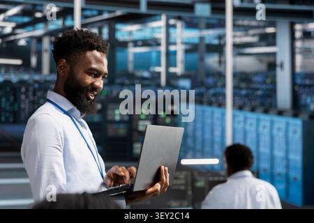 Joyful data center developer monitors system performance on a laptop, finds bottlenecks and troubleshoots glitches for better optimization. Stock Photo