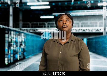 IT technician walking in data infrastructure center with server hardware supporting business needs with african american server facility technical specialist doing checkup. Stock Photo