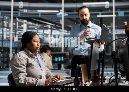 Data center colleagues collaborate on coding and AI automation scripts while reviewing server infrastructure together. Stock Photo