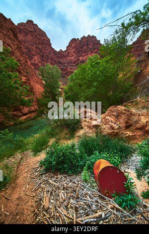 Red Canyon Walls Lush Greenery and Rusted Barrel by Turquoise River in Arizona Stock Photo