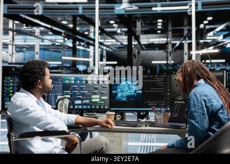 Engineer using a wheelchair works with a colleague to configure AI and machine learning equipment in an inclusive server room. Stock Photo