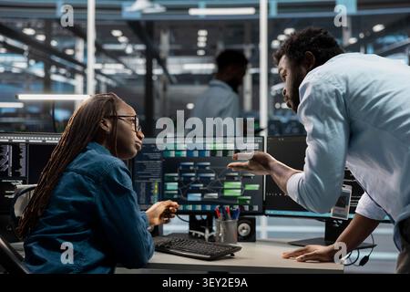 Software developers program data center equipment for machine learning training, discussing code on a PC to upgrade AI systems. Stock Photo
