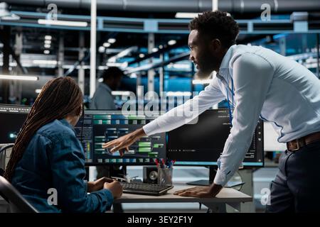 Data center supervisor gives feedback to an engineer programming equipment for machine learning training and AI system upgrades. Stock Photo