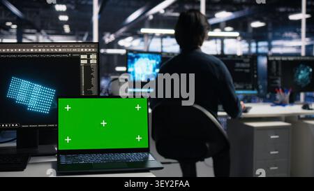 Computer scientist programs on a green screen computer in a data center with generative AI assistance. Stock Photo