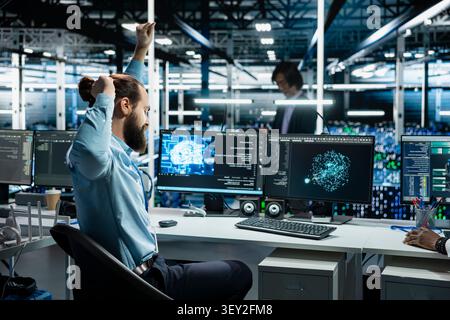 System administrator stretches at a workstation in a server room to relieve back fatigue after long technical work. Stock Photo
