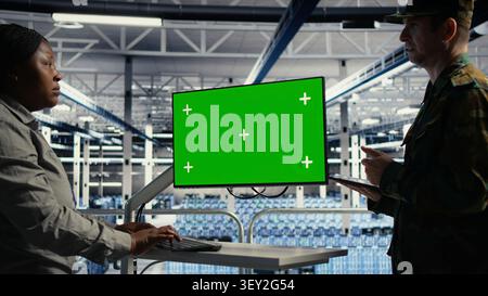 Army experts operate a green screen computer in a server room to deploy AI technology for defense infrastructure. Stock Photo