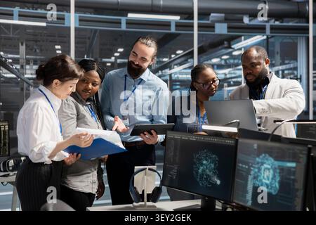 Engineering team collaborating in high tech server room with AI neural network systems tech, while staff members collaborating, working with AI programming language to update equipment. Stock Photo