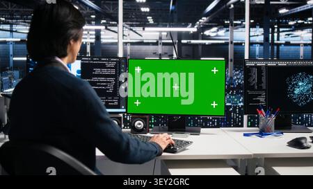 Data center administrator uses green screen PC in a server room to monitor AI diagnostics and neural network performance. Stock Photo