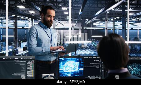 Team supervisor supervising work of server room technical specialist. Stock Photo