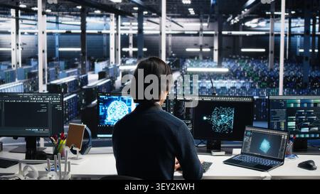 Computing facility system administrator managing AI systems for uptime and efficiency, while IT staff member working with AI technology on computer and notebook in computing hub. Stock Photo