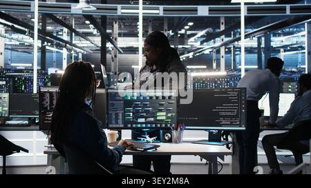 Computing facility team supervisor supervising IT technician working with visual programming system to assess datasets with team leader oversees IT specialist working with visual programming tools. Stock Photo