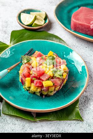 Tuna tartare with mango salad and avocado served on a turquoise plate with lime Stock Photo