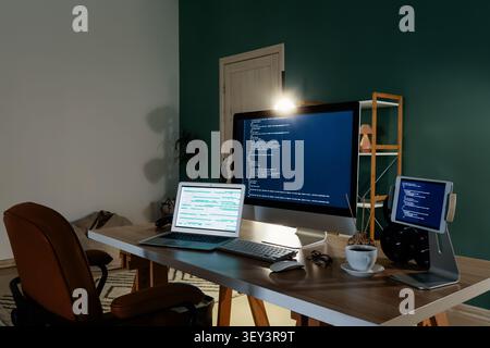 Home office desk with multiple screens displaying code Stock Photo