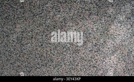 Horizontal close up of beige granite surface with light beige feldspar base, black mineral flecks, white quartz patches, and natural stone texture Stock Photo