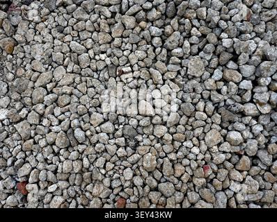 Horizontal close up of gray gravel surface with scattered red stones, red mud spatter, chipped uneven rocks Stock Photo
