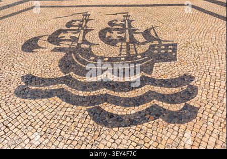 Traditional black and white stone pavement with a sailing ship mosaic in Lisbon, Portugal. Stock Photo