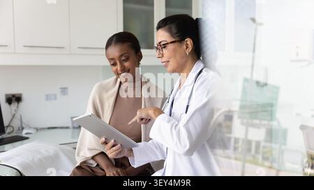 Friendly mature medical professional doctor woman showing tablet to patient Stock Photo