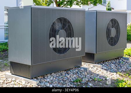 Two modern air to water heat pump units stand outdoors on concrete slabs and gravel next to a residential building, providing sustainable and energy e Stock Photo