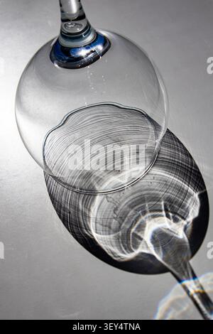 Empty wine glass with blue stem casting circular shadow on grey surface Stock Photo