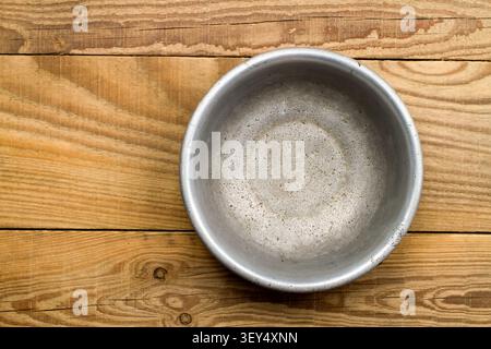 An old aluminum bowl on a background of wood. Close-up aluminum plate. Stock Photo