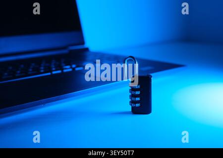 Open combination lock standing in front of a laptop under blue light, symbolizing compromised data security Stock Photo
