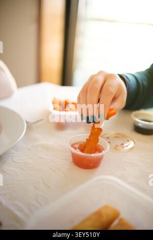 Hand dipping a crunchy fried snack into a small container of sweet chili sauce Stock Photo