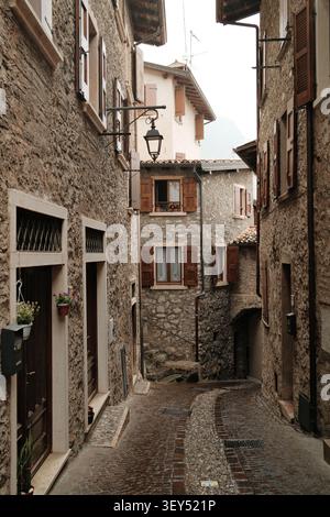 A narrow cobblestone alley lined with traditional stone houses in a lakeside village on Lake Garda, Italy, seen in soft misty morning light Stock Photo