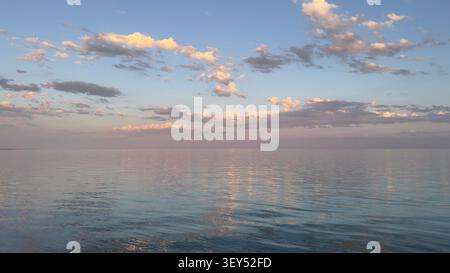 Full moon and golden clouds reflecting on calm sea at dusk.  Stock Photo