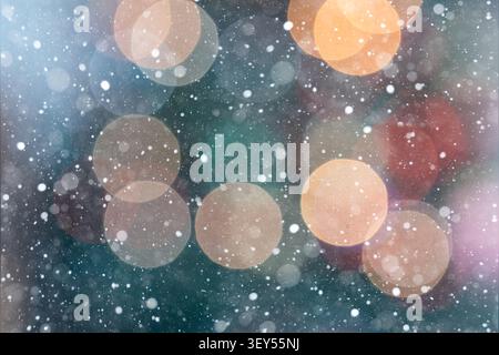 Horizontal abstract festive background with warm red, yellow, orange, and white bokeh lights over a green and brown backdrop. Falling snowflakes creat Stock Photo