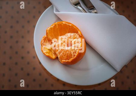 A peeled tangerine sits on a white plate, alongside a folded linen napkin, in Barcelona, Spain. The photograph captures a still life composition with Stock Photo