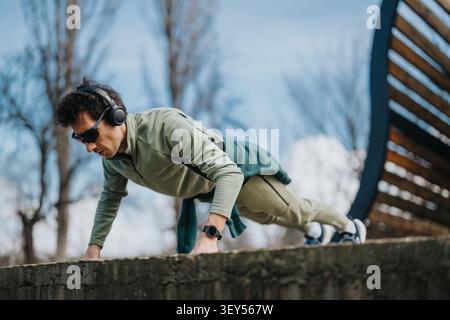 Man doing push-ups outdoors wearing headphones and sunglasses during casual fitness training Stock Photo