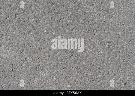 A close-up view of a gray asphalt road surface showing detailed texture, small pebbles, and coarse grain. Ideal for background or construction themes. Stock Photo