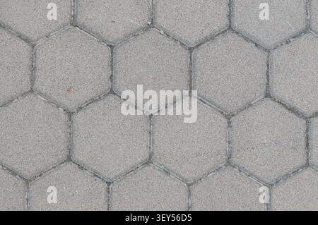A close-up view of gray hexagonal concrete paving stones arranged in a repeating geometric pattern. The texture is coarse-grained and durable for outd Stock Photo