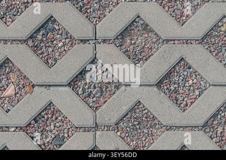 A top-down close-up view of interlocking gray concrete paving blocks with decorative red and gray stone gravel filling the diamond-shaped gaps. Outdoo Stock Photo